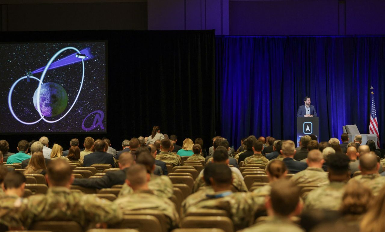 Brad Cheetham presents on the Oracle program to an auditorium of people in US military uniform.